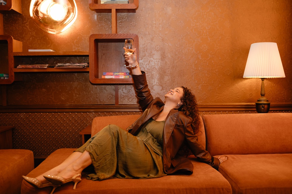 NYC Fashion Week - woman sitting on a couch raising a wine glass up in the air